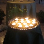 a round tray filled with sand and small, lit tea candles