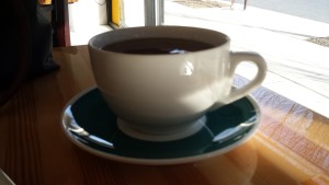 white teacup filled with dark tea on deep green and white saucer