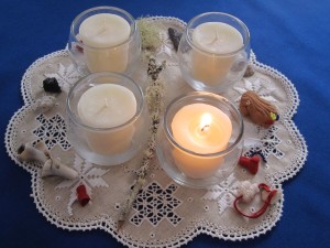 four vigil candles arranged on linen surrounded by tiny read leather pouches, feeather, shell, and other items for Advent wreathit