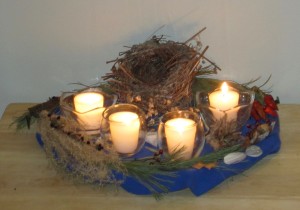 Four beeswax vigil candles in glass holders, surrounded by birds nest and other natural objects used as an Advent wreath